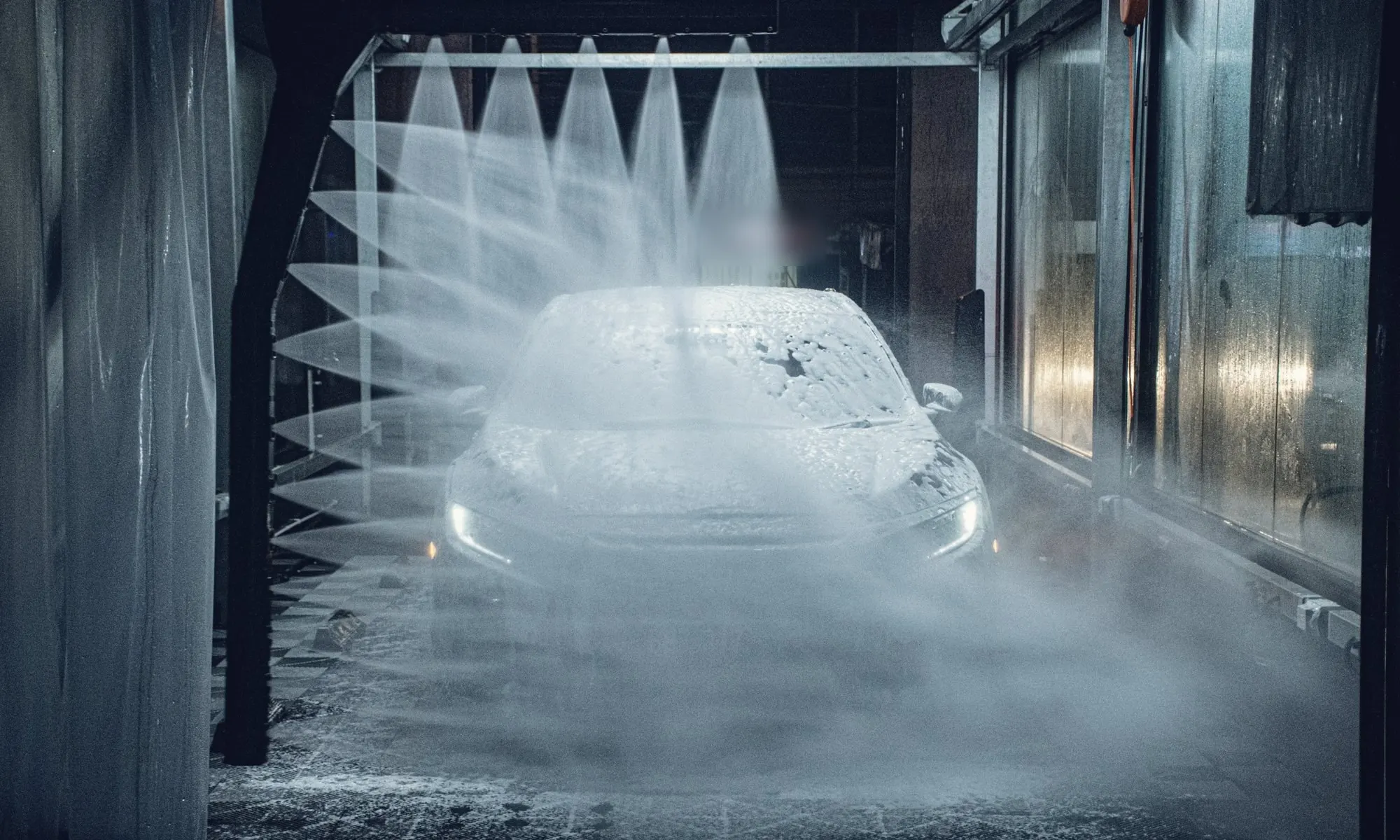 A car covered in foam under high-pressure water jets inside an automatic car wash.
