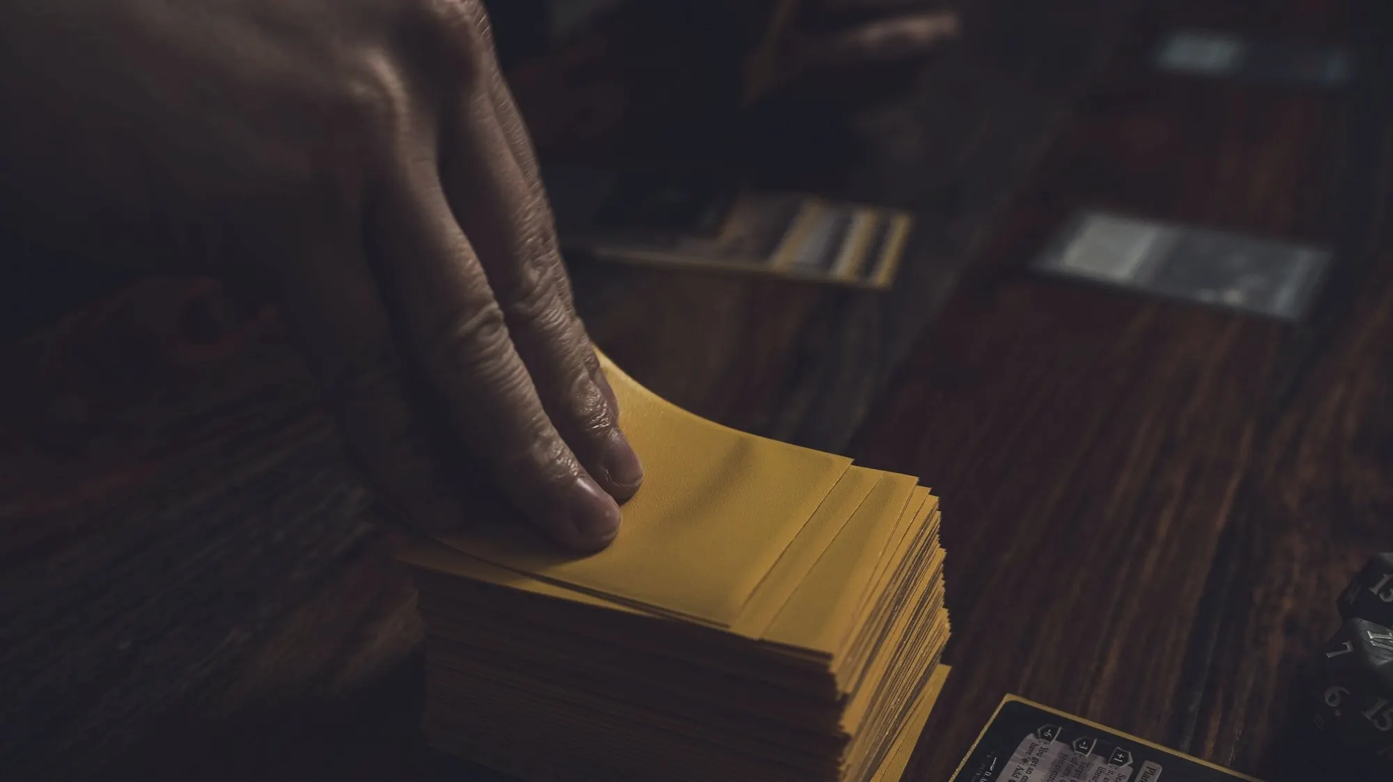 Hands shuffling a stack of sleeved trading cards on a wooden table.