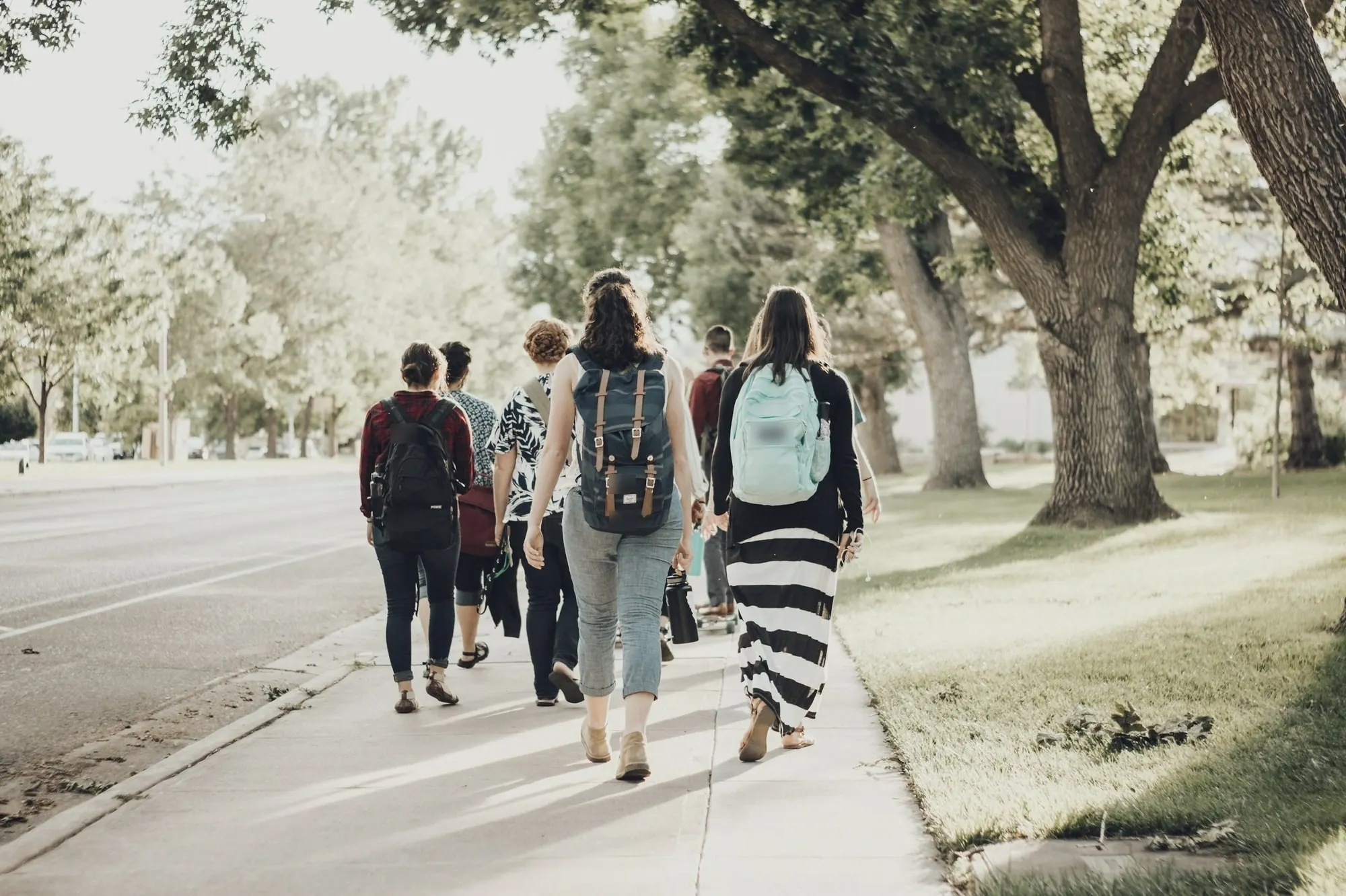 A group of students with backpacks walking along a tree-lined sidewalk.