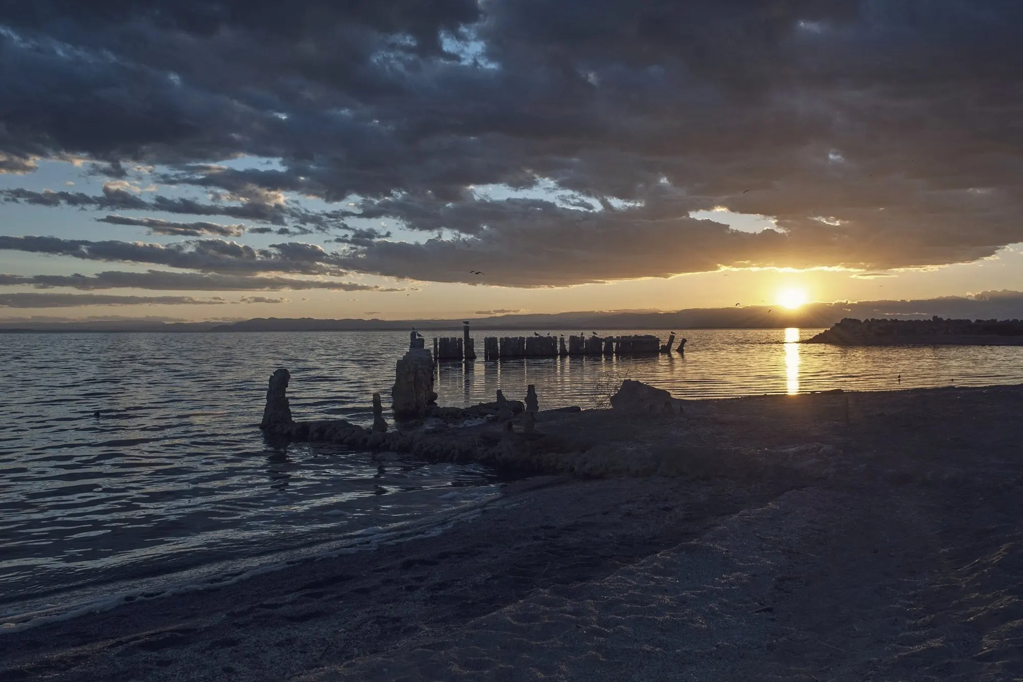 Sunset over the Salton Sea shoreline with old pilings rising from the water.