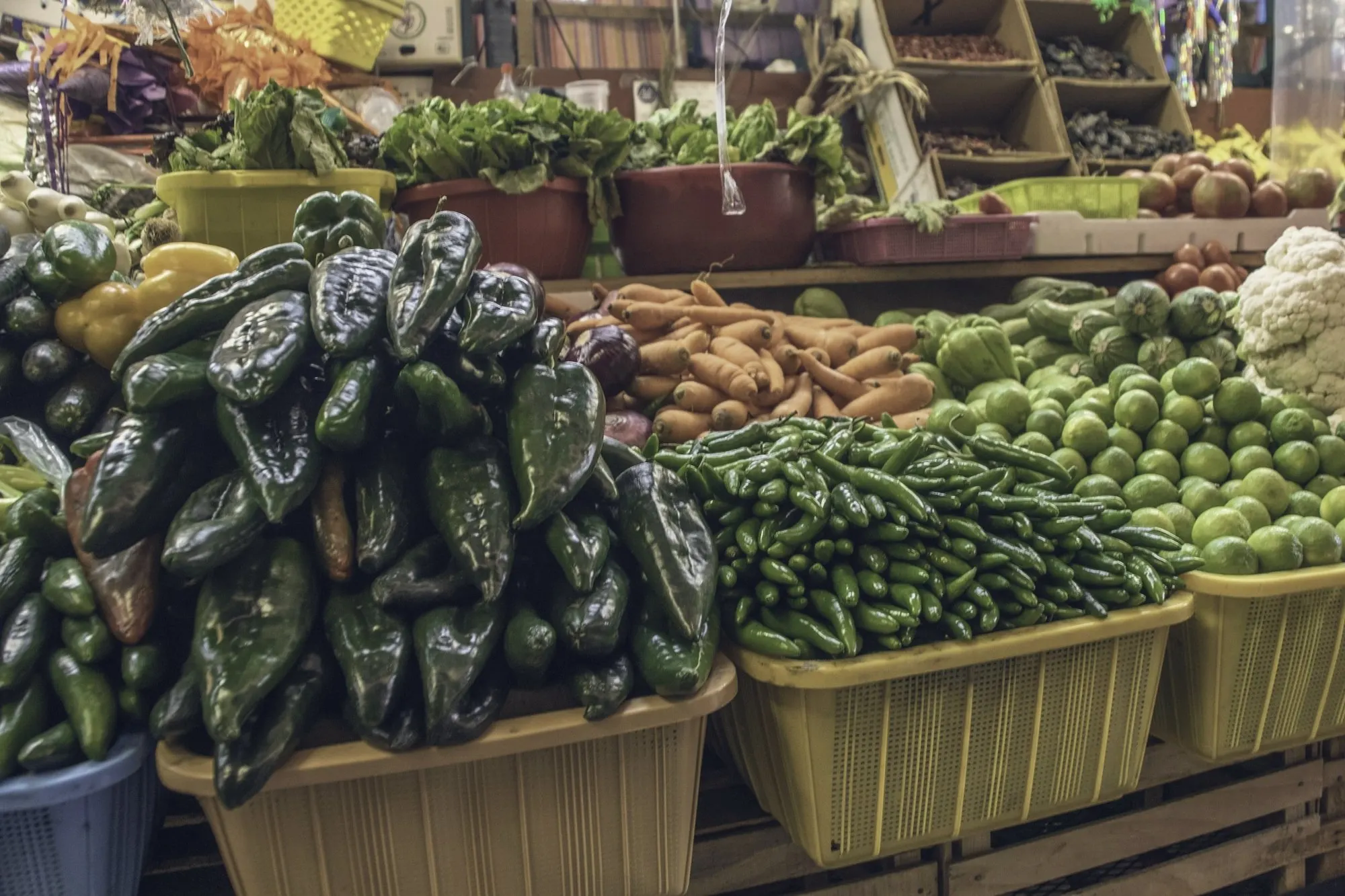 Baskets piled with fresh chiles, limes and vegetables at a market produce stand.