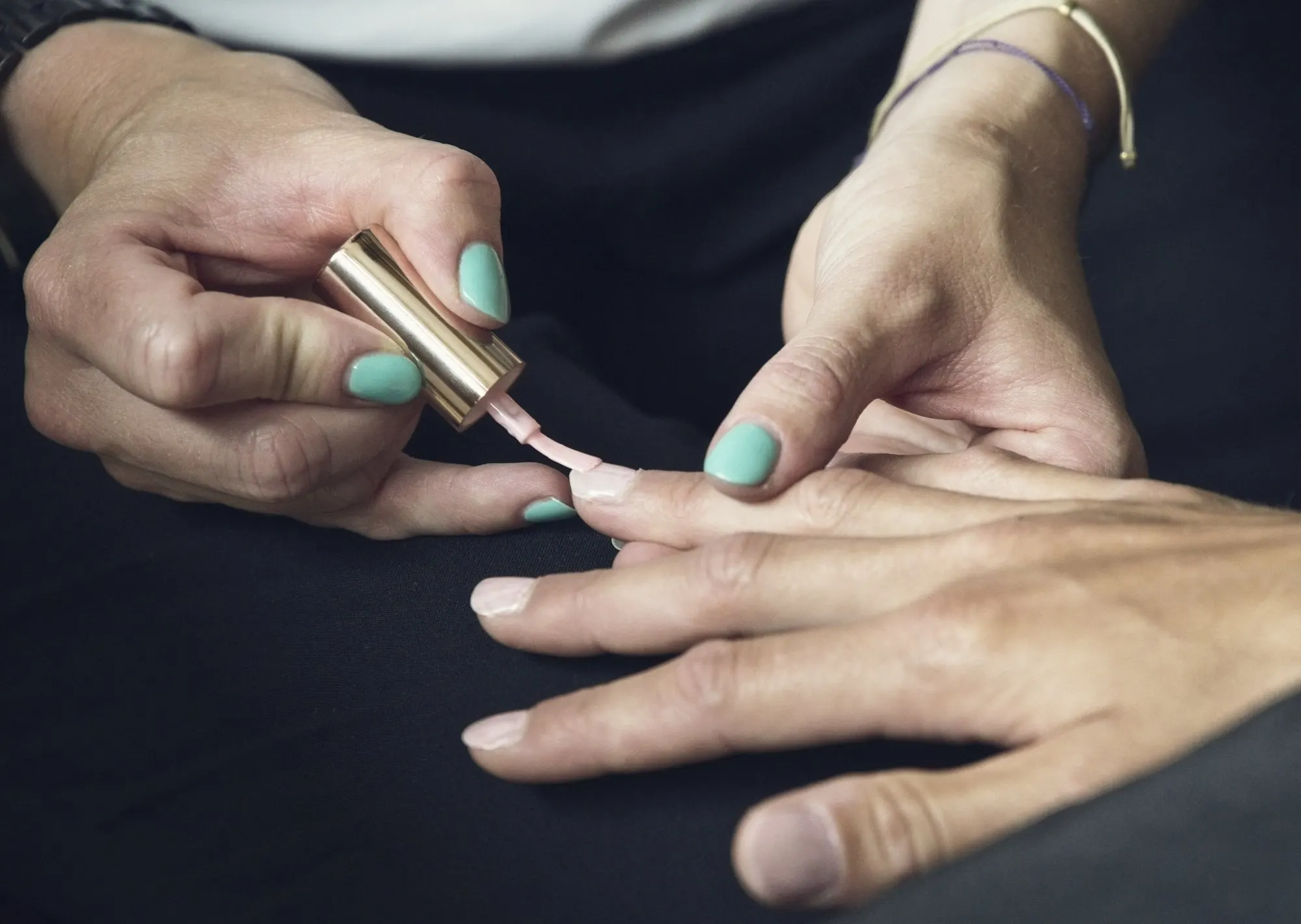 Close-up of hands applying pale polish to fingernails during a manicure.