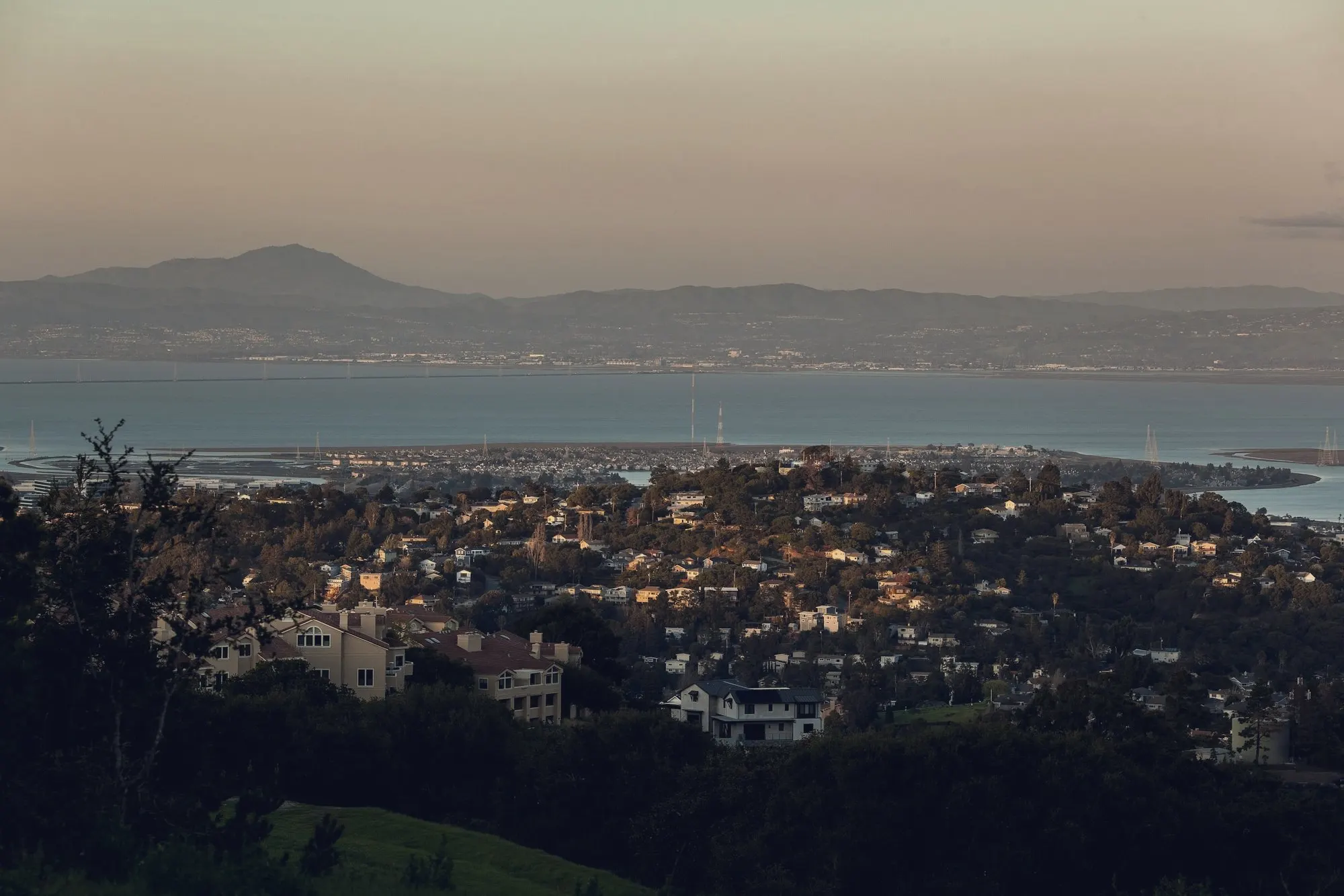 Hillside neighborhood overlooking San Francisco Bay and distant mountains at golden hour.