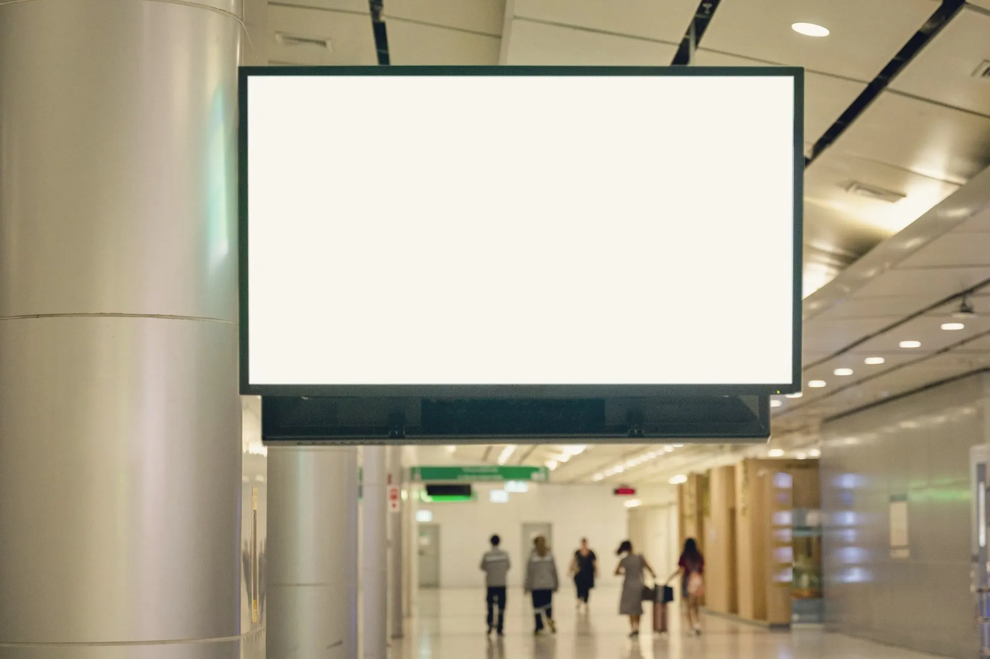 A large blank white display screen hangs above a bright indoor shopping concourse.