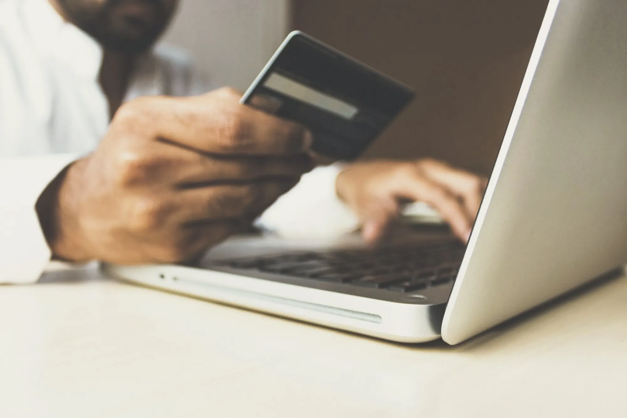 A hand holds a payment card while typing on a laptop keyboard at a desk.