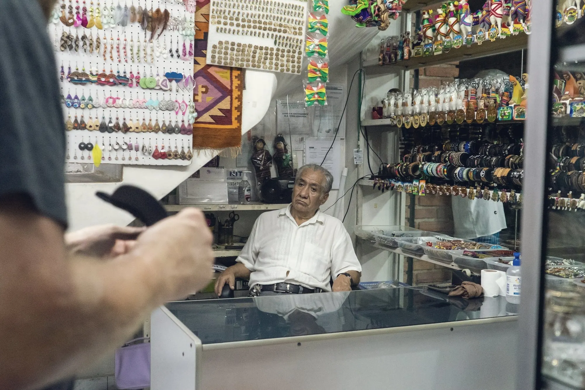 A shopkeeper behind a glass counter in a small crowded store.