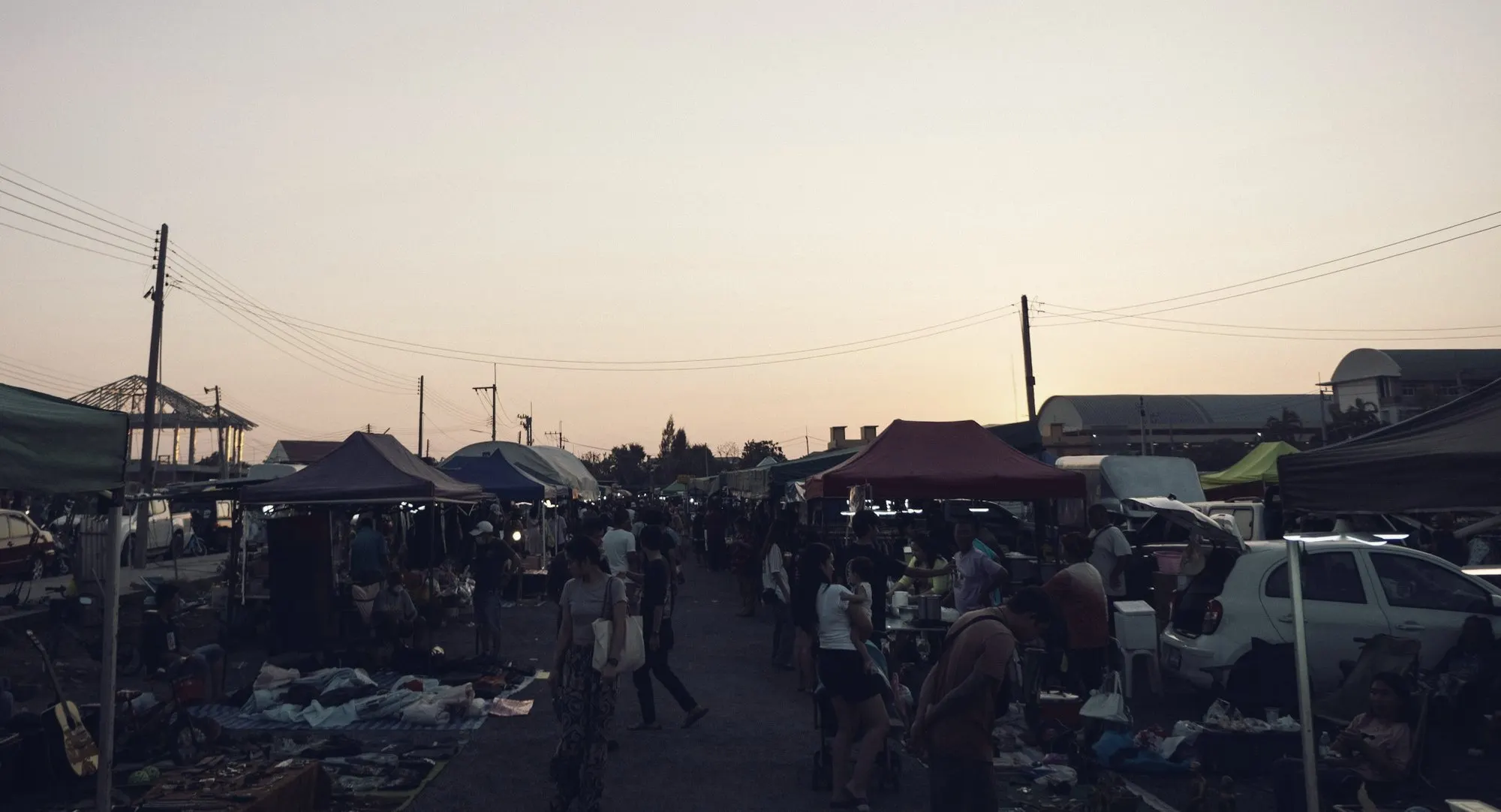 Shoppers browsing tables and canopy stalls at an outdoor flea market at dusk.